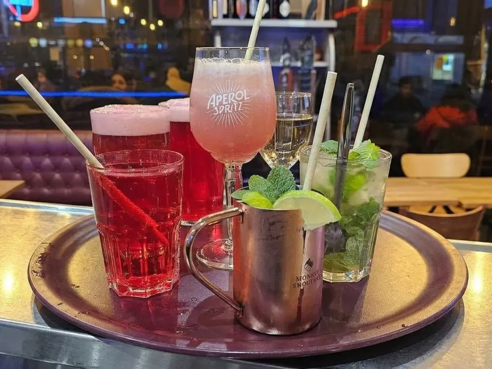 Plateau de cocktails servi au comptoir en soirée : Aperol Spritz, Moscow Mule et mojito